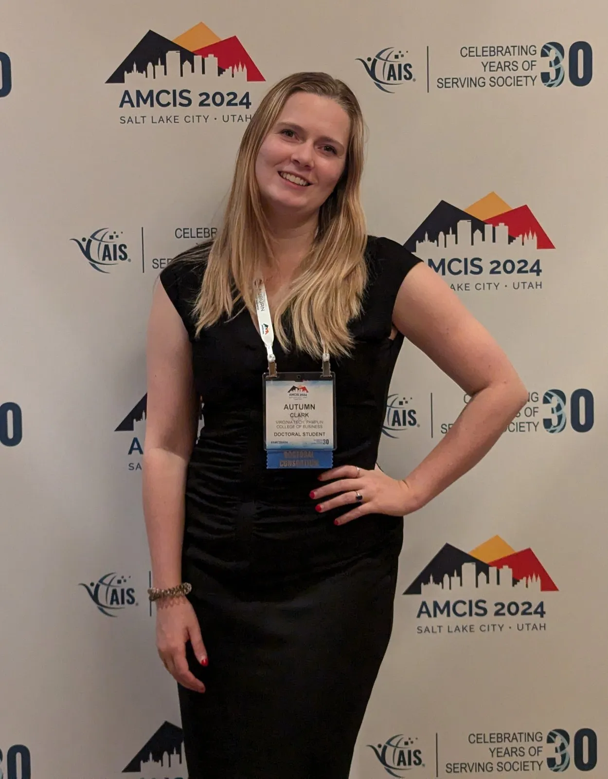 Autumn Clark wearing a doctoral student badge in front of an AMCIS 2024 Salt Lake City backdrop.