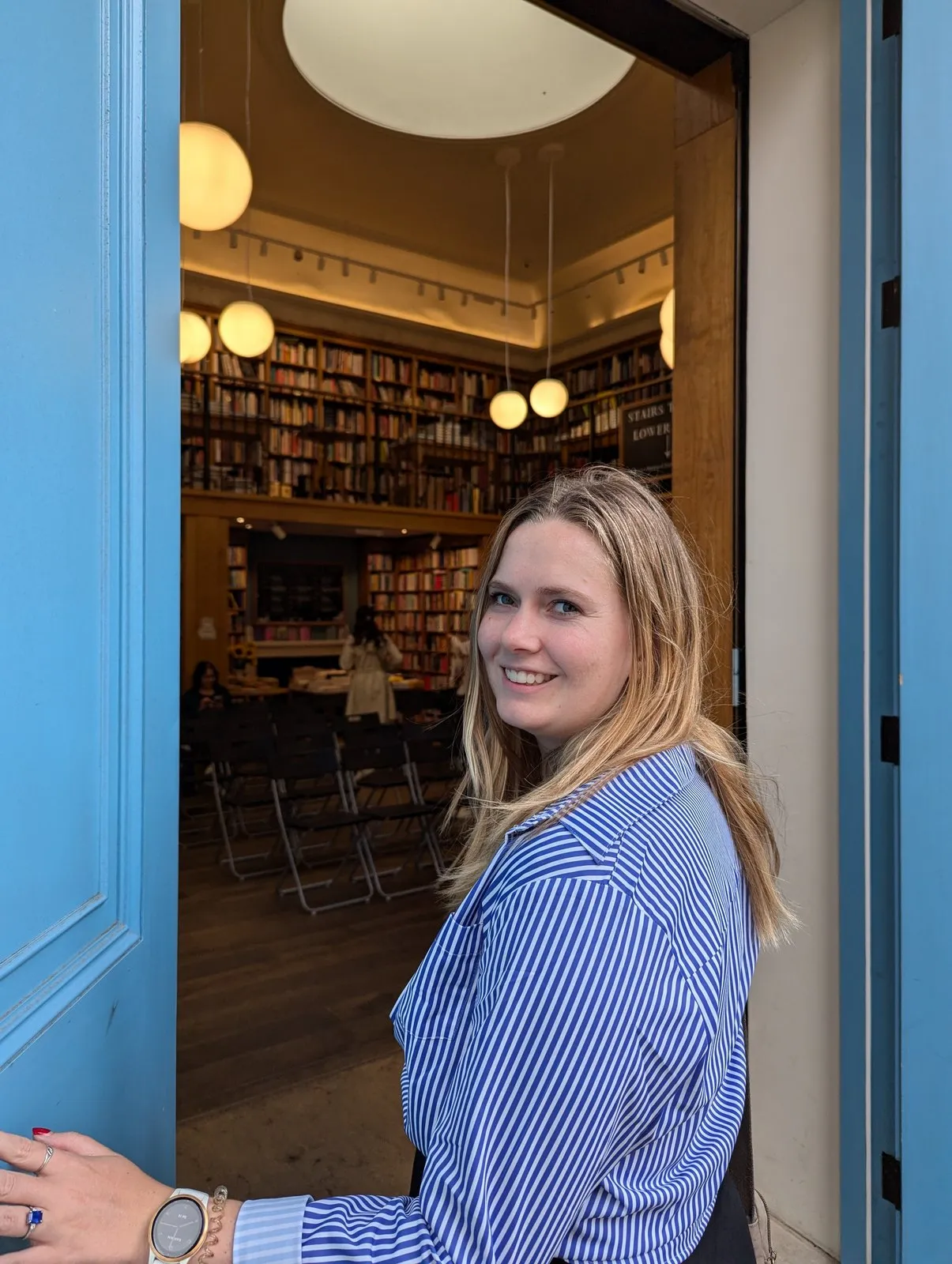 Autumn Clark smiling in the open blue doorway of a bookshop lined with shelves.