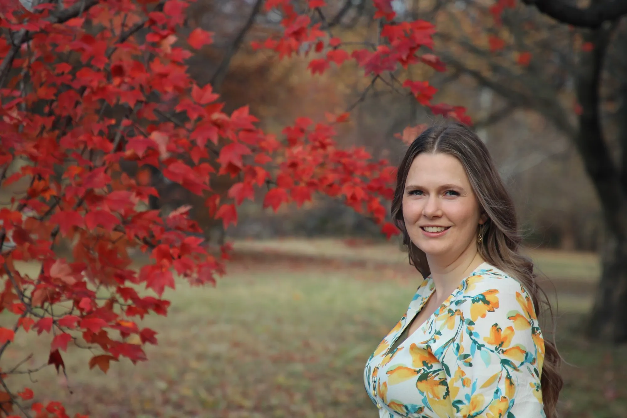 Autumn Clark outdoors in autumn, beneath a maple tree with red leaves.